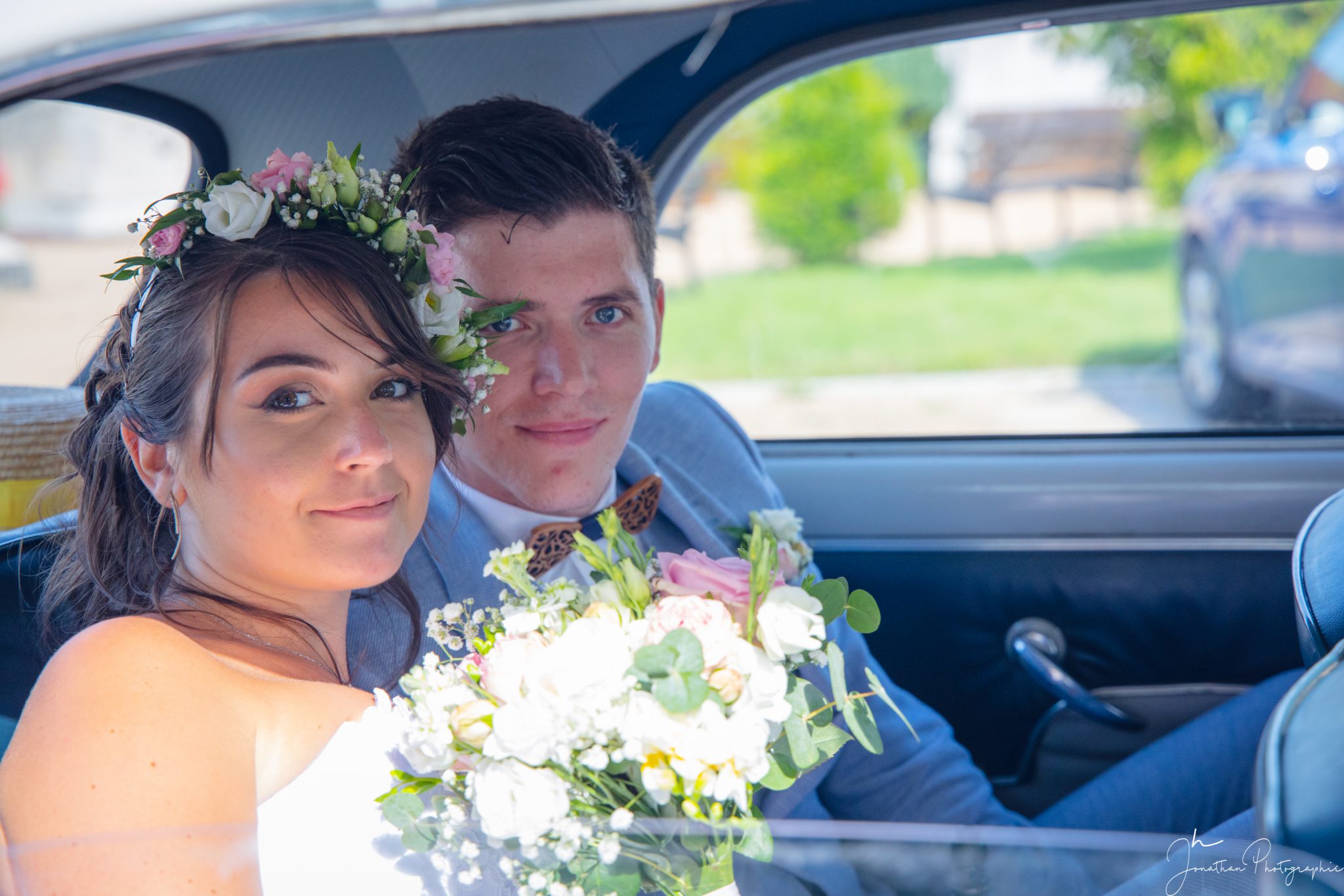 Photo des mariés réunis à l'arrière de la voiture, bouquet à la main