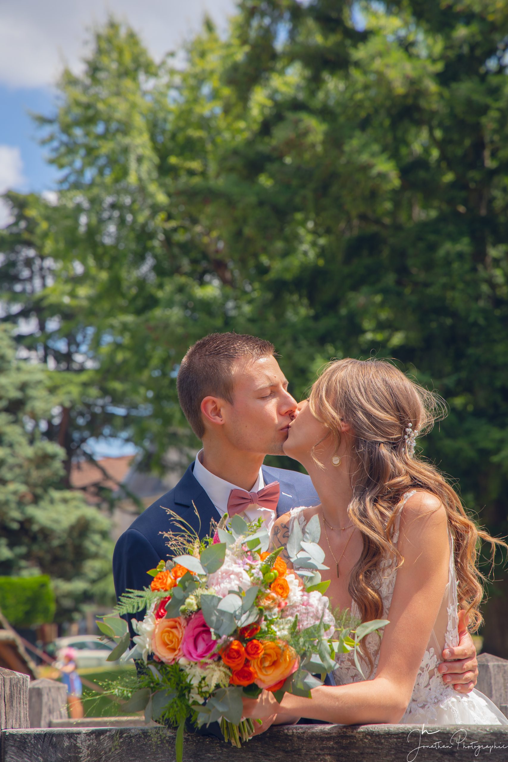 Couple de mariés qui s'embrassent avec le bouquet de fleurs à la main