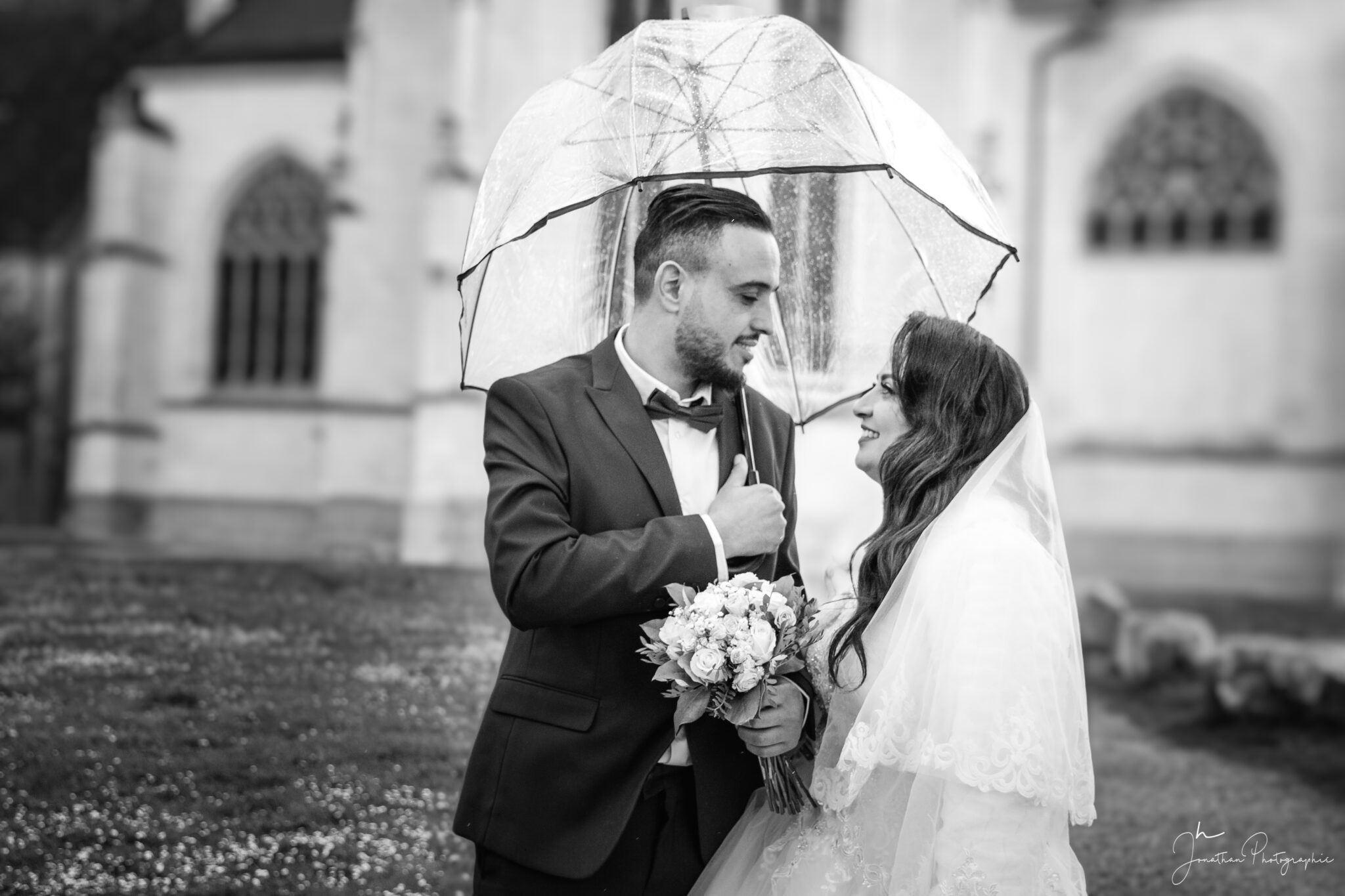 Photo en noir et blanc avec les deux mariés sous un parapluie