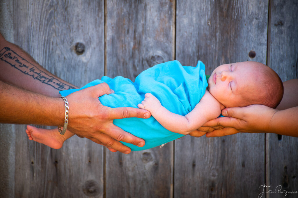 Séance photo d'un bébé porté par ses parents aux extrémités sur fond en bois